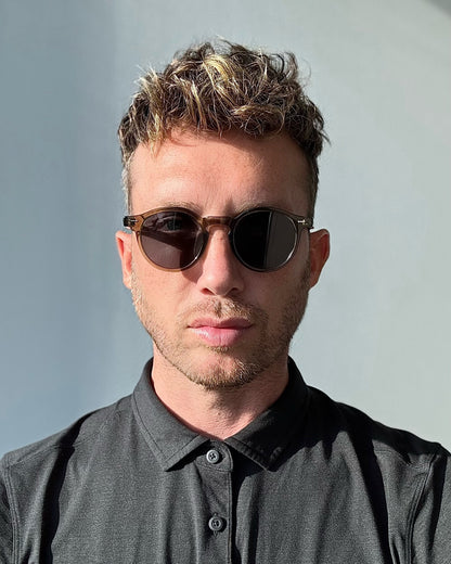 Man wearing green sunglasses and a dark shirt against a light background