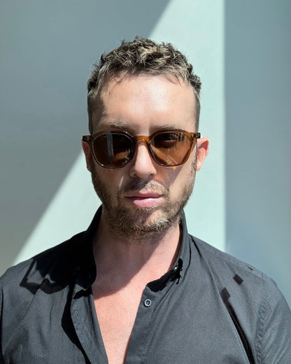 Man wearing sunglasses and a dark shirt against a light background