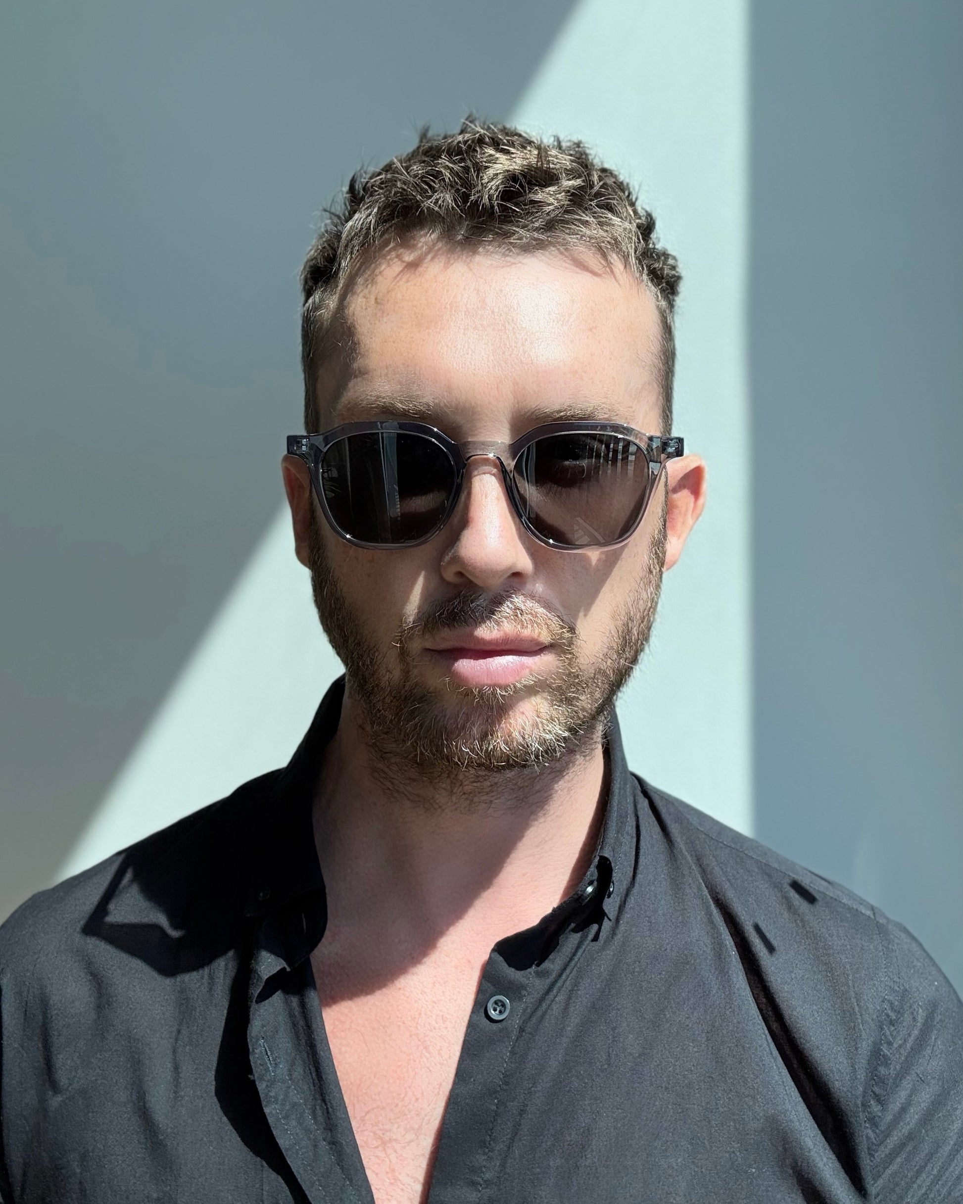 Man wearing sunglasses and a black shirt against a light background