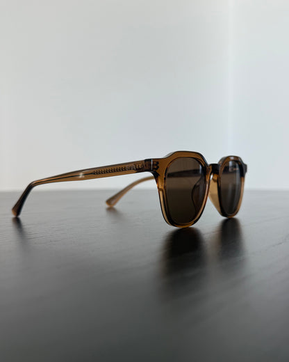 Sunglasses with brown frame and dark lenses on a reflective surface with a light gray background