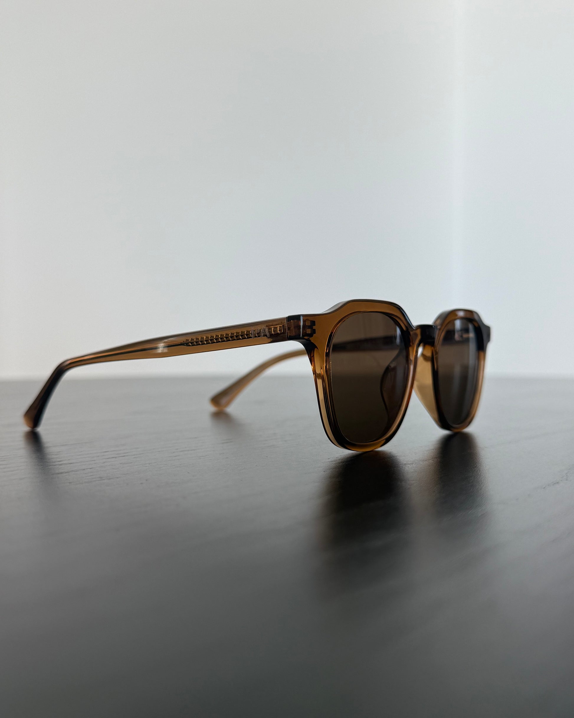 Sunglasses with brown frame and dark lenses on a reflective surface with a light gray background