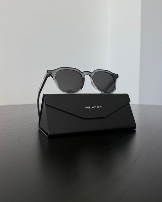 Grey sunglasses with a black case on a reflective surface