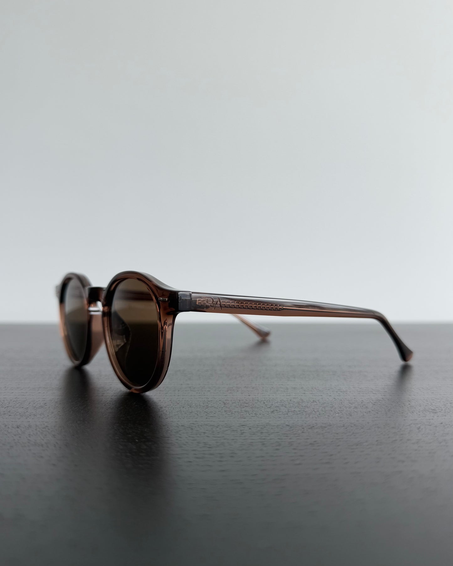 Round sunglasses with brown gradient lenses on a dark surface with a light gray background