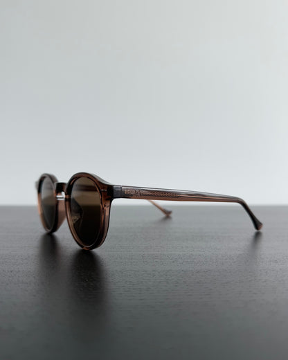 Round sunglasses with brown gradient lenses on a dark surface with a light gray background