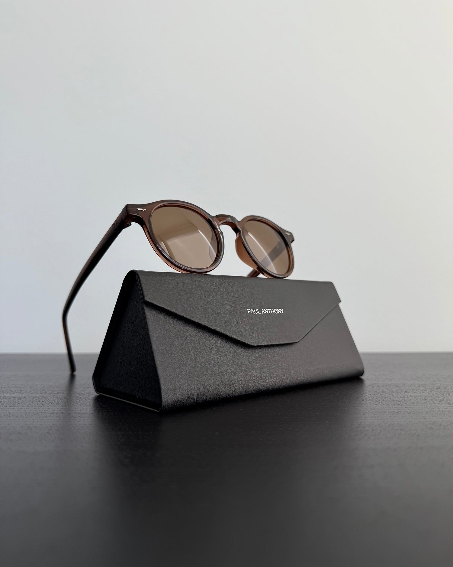 Sunglasses on a black carrying case with 'Paul Andrew' branding on a dark surface.