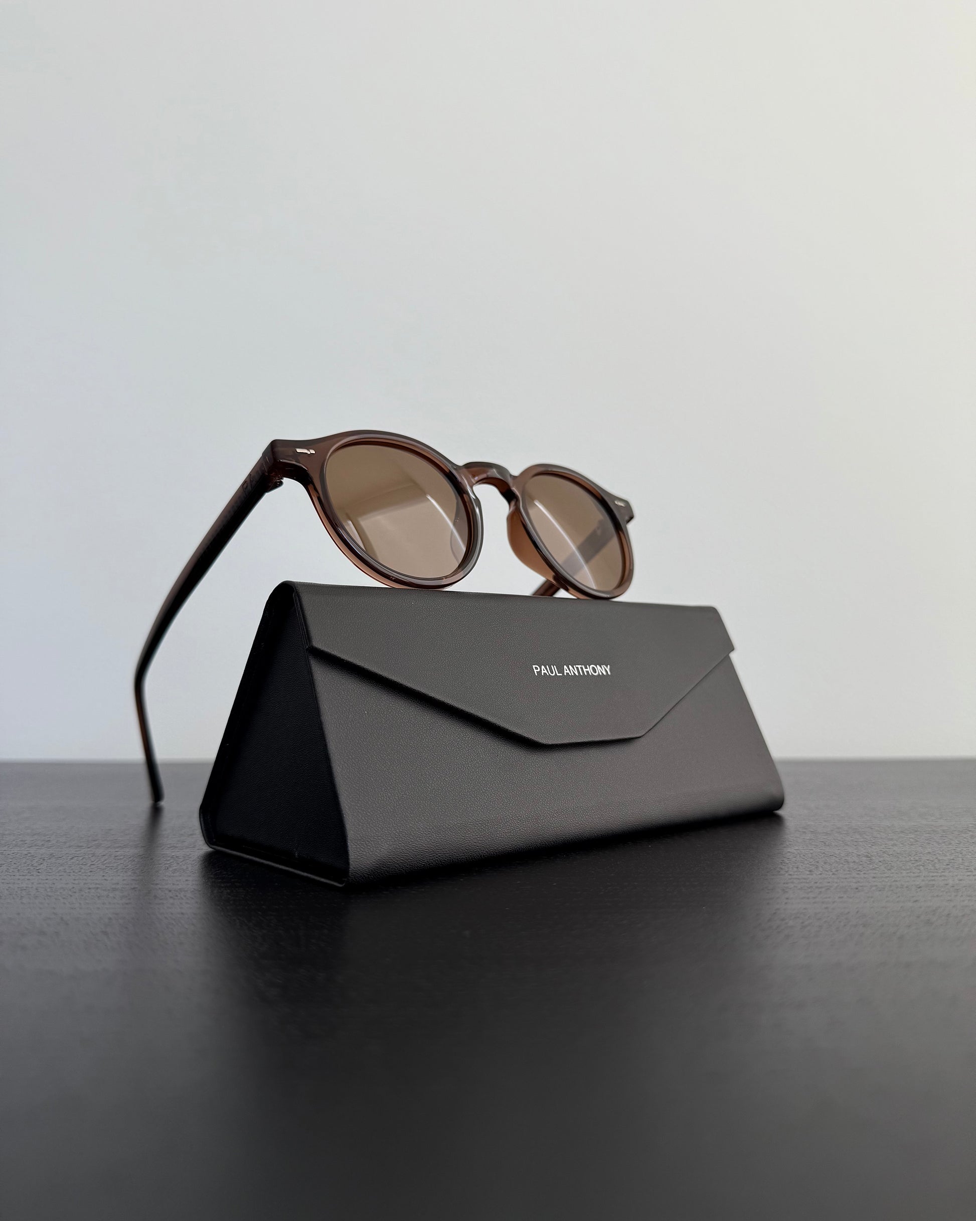 Sunglasses on a black carrying case with 'Paul Andrew' branding on a dark surface.